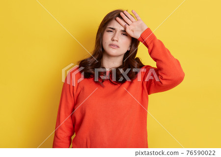 Tensed woman touching her head and looking directly at camera with tired painful look, dresses orange jumper isolated over yellow background, having problem with health. Tensed woman touching her head and looking directly at camera with tired painful look, dresses orange jumper isolated over yellow background, having problem with health. 76590022