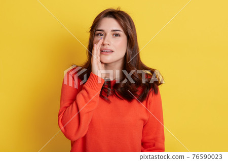 Photo of pretty dark haired lady sharing new information, holding arm near mouth, wearing orange sweater isolated yellow background, girl gossiping with somebody. Photo of pretty dark haired lady sharing new information, holding arm near mouth, wearing orange sweater isolated yellow background, girl gossiping with somebody. 76590023