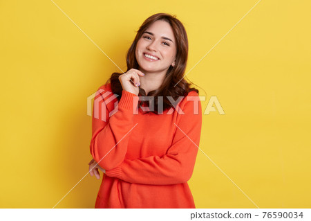 Happy smiling dark haired woman with pleasant appearance, wearing casually, looking at camera with toothy smile, keeping fist under chin, standing isolated over yellow background. Happy smiling dark haired woman with pleasant appearance, wearing casually, looking at camera with toothy smile, keeping fist under chin, standing isolated over yellow background. 76590034