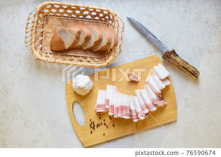 Flat lay composition of traditional Ukrainian food, knife, bread box with dark bread slices, garlic, peppercorn, slices of salo, appetizer, feeling of hunger, delicious snack. Traditions concept. 76590674