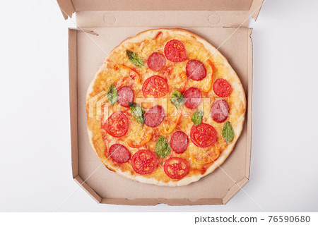 Top view of delicious hot pizza in box with ham and tomatoes sliced and served on white table, tasty supper for fast food lovers on light surface, box with pizza isolated over white background. Top view of delicious hot pizza in box with ham and tomatoes sliced and served on white table, tasty supper for fast food lovers on light surface, box with pizza isolated over white background. 76590680