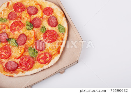 Top view of hot tasty pizza in box with ham sliced and served on white table, close up view. Fast food, junk food and nhealthy eating concept. Copy space for promotion text or your advertisment. 76590682