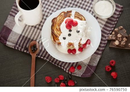 Tasty pancakes with blueberries and raspberries on cotton towel on dark table, cup of tea or coffe, spoon, pieces of chocholate, spoon. Delicious pancackes for breakfast, muffins woth bresh berries. 76590750