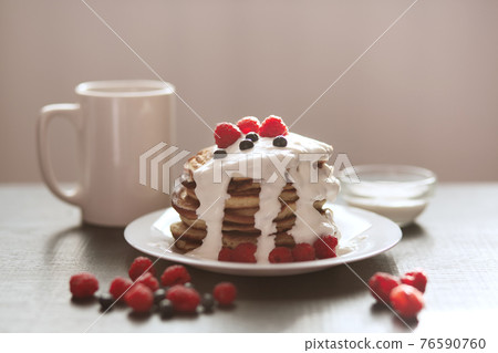 Top view of fresh baked muffins for breakfast in white plate, decorated with sour cream and berries, plate with pancackes and cup of tea, raspberries and blueberries. Delicious breakfast concept. 76590760