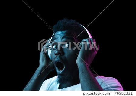 Close up young African-American man isolated on dark background in neon light 76592331