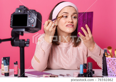 Close up portrait of young Caucasian woman blogger, advertising new eyeshadow for her followers, online translation, lady looks at mirror, makes tutorial video for beauty vlog. Vlogging concept. Close up portrait of young Caucasian woman blogger, advertising new eyeshadow for her followers, online translation, lady looks at mirror, makes tutorial video for beauty vlog. Vlogging concept. 76592862