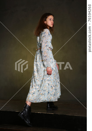 model girl in long printed dress and black boots full body portrait walking on dark wall background 76594268