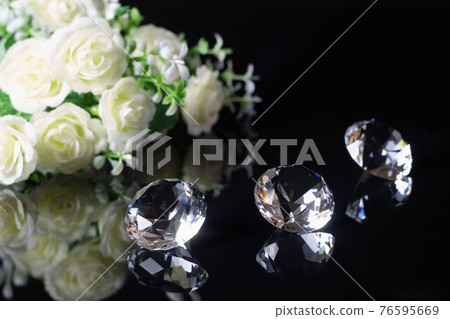 Three excellent diamonds of the first water and bouquet of white roses with reflection on black mirror background close up view. Jewelry diamonds sale, invitation, discount poster template Three excellent diamonds of the first water and bouquet of white roses with reflection on black mirror background close up view. Jewelry diamonds sale, invitation, discount poster template 76595669