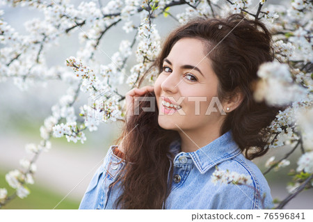 Beautiful happy girl with spring flowers. Portrait of young smiling brunette woman outdoor. 76596841