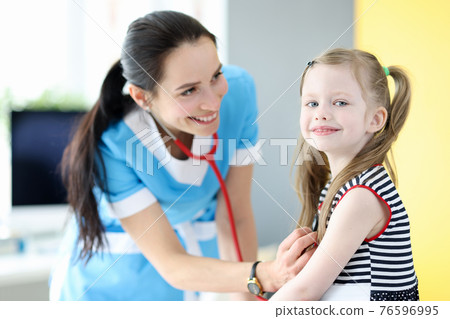 Smiling doctor listens with stethoscope to breathing of little girl 76596995
