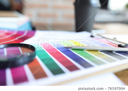 Color palette with pen and magnifying glass is on table 76597004