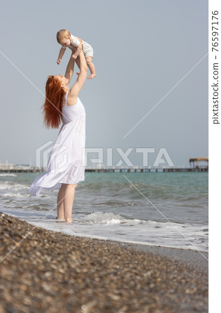 Happy woman raising up her little son standing on the beach above the sea Happy woman raising up her little son standing on the beach above the sea 76597176