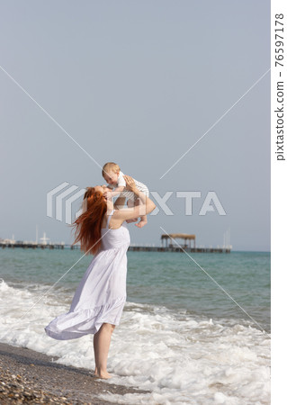 Happy mother raising up her little son standing on the beach above the sea Happy mother raising up her little son standing on the beach above the sea 76597178