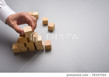 Businessman arranging wooden cubes in pyramid shape 76597404