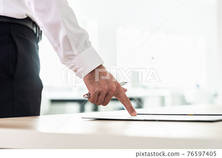 Businessman standing at his office desk pointing to a document Businessman standing at his office desk pointing to a document 76597405