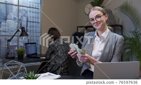 Businesswoman receiving money cash income from laptop in office after successful financial deal Businesswoman receiving money cash income from laptop in office after successful financial deal 76597636
