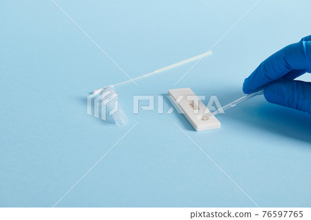 A hand in a protective medical glove drips a reagent into a test strip and makes a test for covid-19 on a blue background. Copy space 76597765