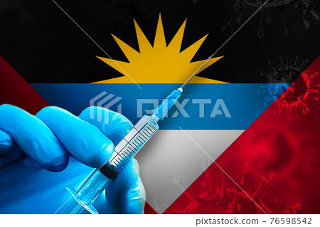 Antigua and Barbuda Covid-19 Vaccination Campaign. Hand in a blue rubber glove holds a syringe with covid-19 virus vaccine in front of flag 76598542