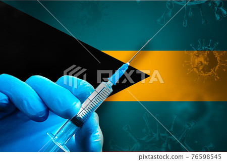 Bahamas Covid-19 Vaccination Campaign. Hand in a blue rubber glove holds a syringe with covid-19 virus vaccine in front of Bahamas flag 76598545