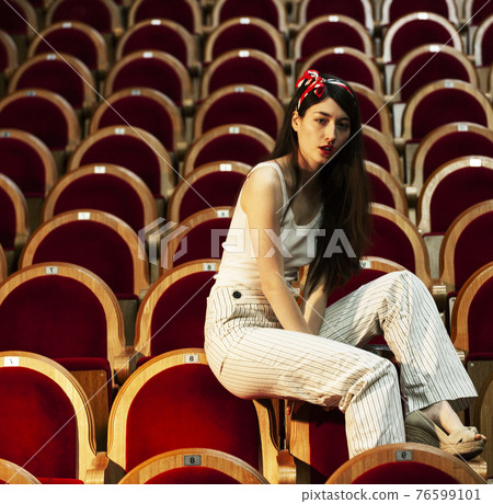 portrait of a pretty girl hipster in a movie theater wearing hat, dreaming alone, fashion lufestyle people concept portrait of a pretty girl hipster in a movie theater wearing hat, dreaming alone, fashion lufestyle people concept 76599101