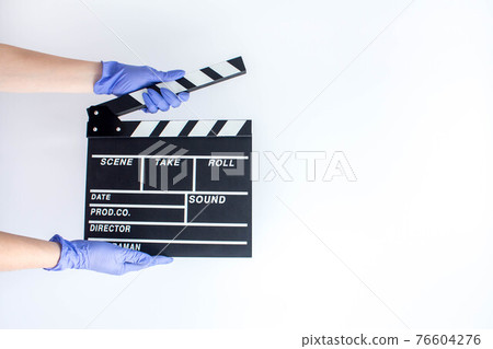 Hands in blue disposable rubber gloves holding movie clapper. Influence of pandemic on cinematography 76604276
