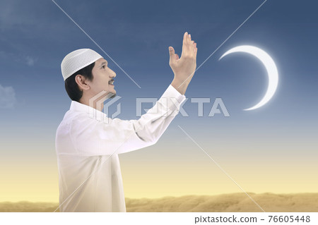 Asian Muslim man standing while raised hands and praying Asian Muslim man standing while raised hands and praying 76605448