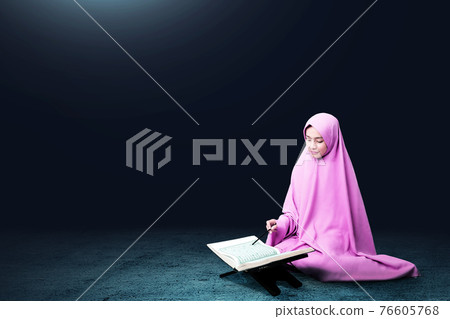 Asian Muslim woman in a veil sitting and reading the Quran Asian Muslim woman in a veil sitting and reading the Quran 76605768