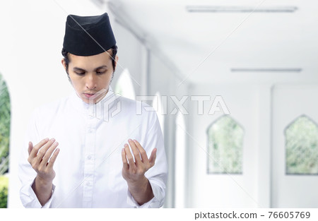 Asian Muslim man standing while raised hands and praying Asian Muslim man standing while raised hands and praying 76605769
