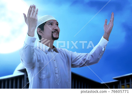 Asian Muslim man standing while raised hands and praying Asian Muslim man standing while raised hands and praying 76605771