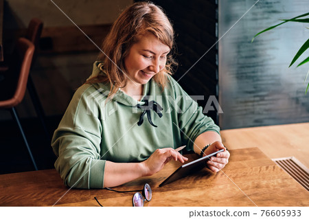 Long-haired woman draws on tablet and smiles at cafe table. Selective focus 76605933