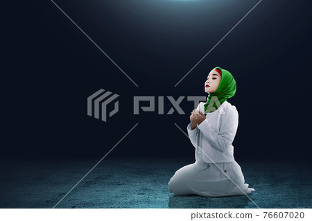 Asian Muslim woman in a veil sitting while raised hands and praying 76607020