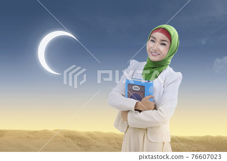 Asian Muslim woman in a veil standing and holding the Quran 76607023