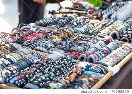Background with a wide variety of imitation jewelry decorative bracelets, souvenirs, hand made personal beauty accessories sold on a tray in the market 76608229