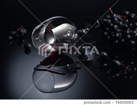 Blue grapes and wine glass with red wine on a black reflective background. Blue grapes and wine glass with red wine on a black reflective background. 76609002
