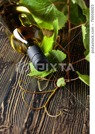 An unopened bottle of white wine and grapevine on an old wooden table. An unopened bottle of white wine and grapevine on an old wooden table. 76609003