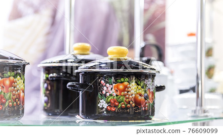 Dishes for cooking, kitchen tools, household goods. Enamelled black pans with a pattern are stored on a shelf in a home interior Dishes for cooking, kitchen tools, household goods. Enamelled black pans with a pattern are stored on a shelf in a home interior 76609099