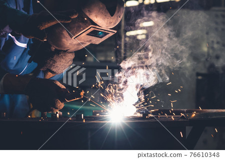 Skillful metal worker working with arc welding machine in factory 76610348