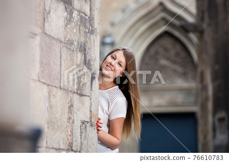 Young woman looking out from behind stone wall 76610783