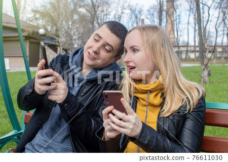 Man and a woman are both sitting on a date and sipping into their smartphones. Concept of social media addiction, getting out of reality and ignoring each other. Couple sitting on a swing in the park Man and a woman are both sitting on a date and sipping into their smartphones. Concept of social media addiction, getting out of reality and ignoring each other. Couple sitting on a swing in the park 76611030