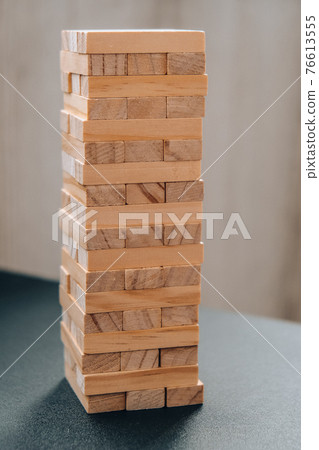 Building from wooden blocks. Game for family of wooden bars. Wood blocks stack game with Hand on background. Block tower with architecture model. 76613555