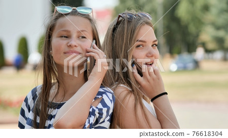 Two young girls talking on the phone on a summer day. Two young girls talking on the phone on a summer day. 76618304