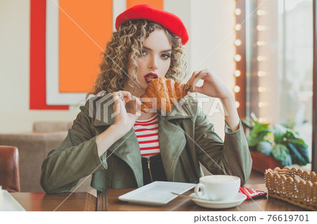 Pretty woman drinking coffee, eating croissant and relaxing in cafe 76619701