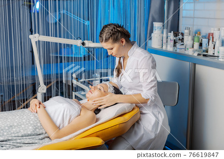 Professional beautician makes a facial massage to Professional beautician makes a facial massage to 76619847