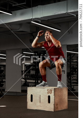 Sexy muscular men using the platform for his legs on a dark colorful background of gym. Sexy muscular men using the platform for his legs on a dark colorful background of gym. 76622711
