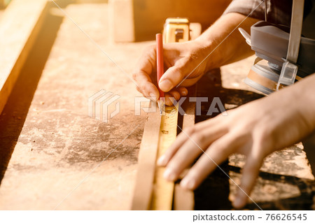 Carpenter man working in furniture wood workshop, Closeup hand measuring and mark on wooden piece. 76626545