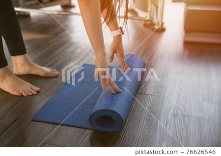 Healthy woman rolling preparing yoga mat for fitness class Healthy woman rolling preparing yoga mat for fitness class 76626546