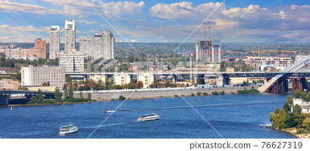 Panoramic cityscape of the Dnipro with cruising pleasure boats against the background of the Kyiv embankment, bright beautiful sky and city buildings. Panoramic cityscape of the Dnipro with cruising pleasure boats against the background of the Kyiv embankment, bright beautiful sky and city buildings. 76627319