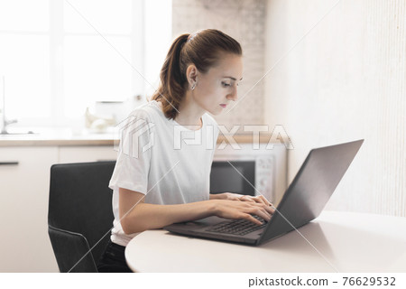 Young woman working on laptop at kitchen. Female freelancer working online 76629532