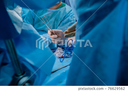 Bloodied surgeon's hands in sterile latex gloves holding surgical tweezers with traces of blood.  76629562