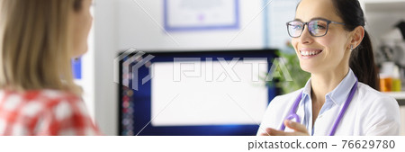 Smiling doctor talking to patient at table in clinic 76629780